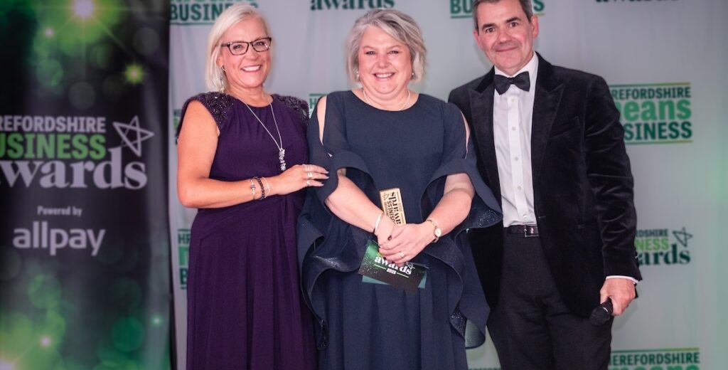 Becky Wall BEM, founder of A Plush Flush and owner of Loo of the Year Awards, who was recently named Entrepreneur of the Year 2025 at the Herefordshire Means Business Awards. Image shows her in the centre being presented with her award.